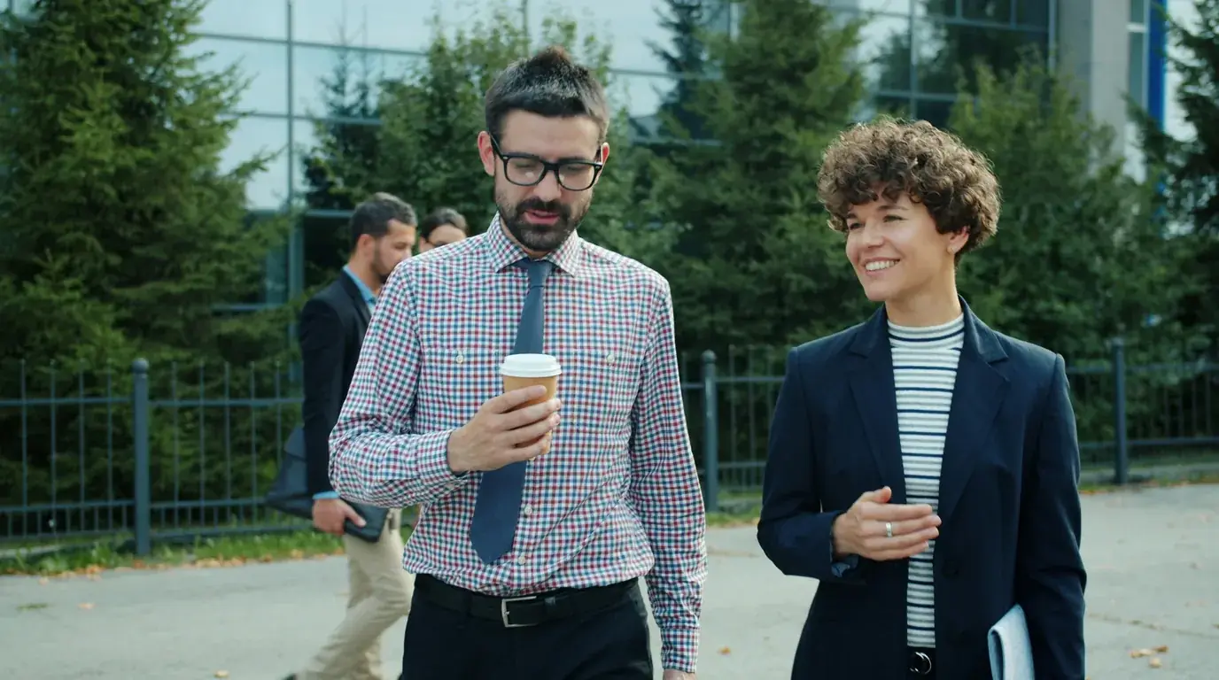 Two colleagues walking and talking outside an office, one holding a coffee