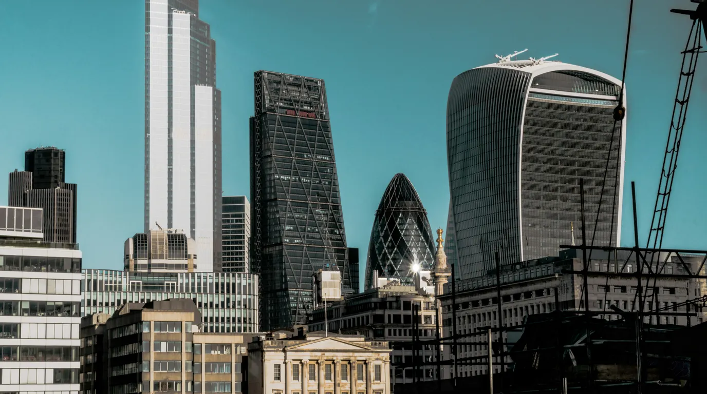 A skyline of glass office towers, one curved and one lattice-clad, sharp against a deep teal sky with crane cables at the right.