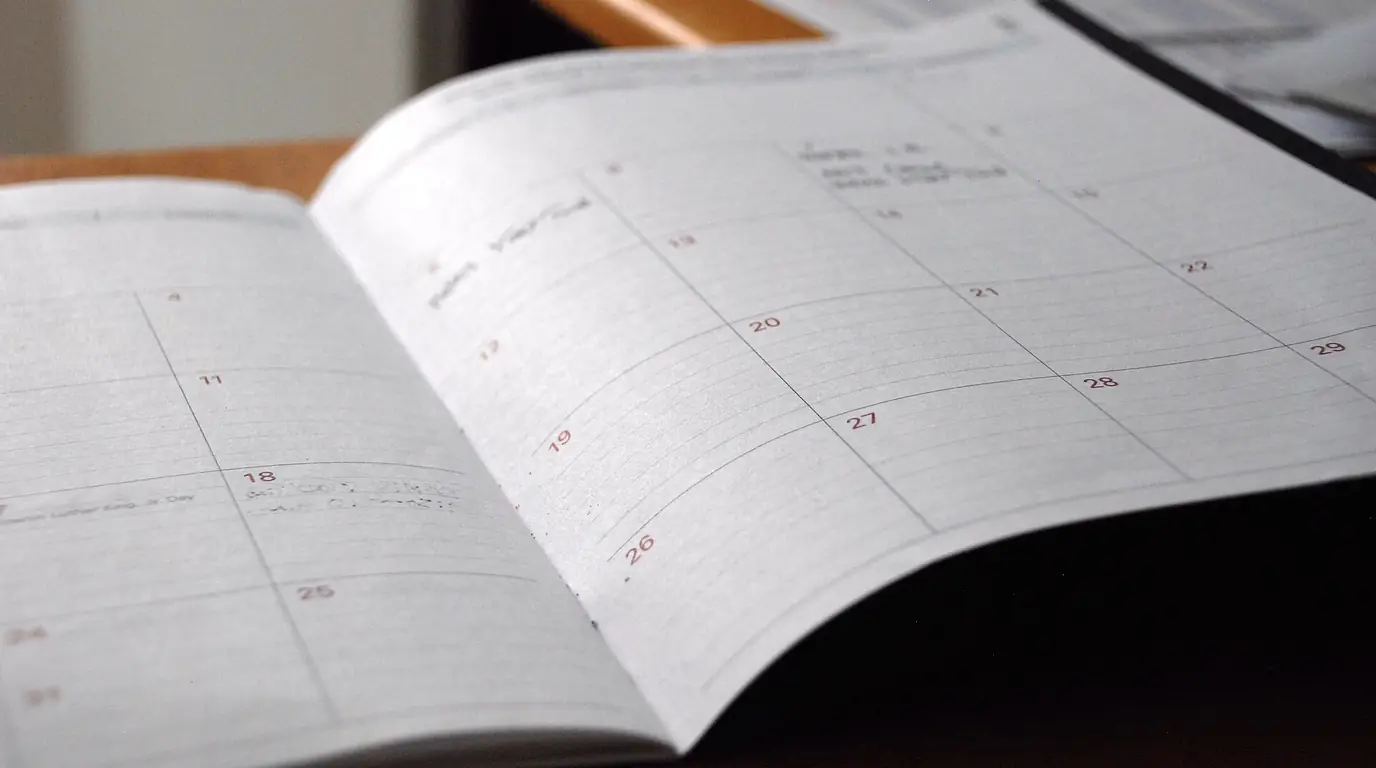 An open paper planner on a desk showing a month grid with a few handwritten entries