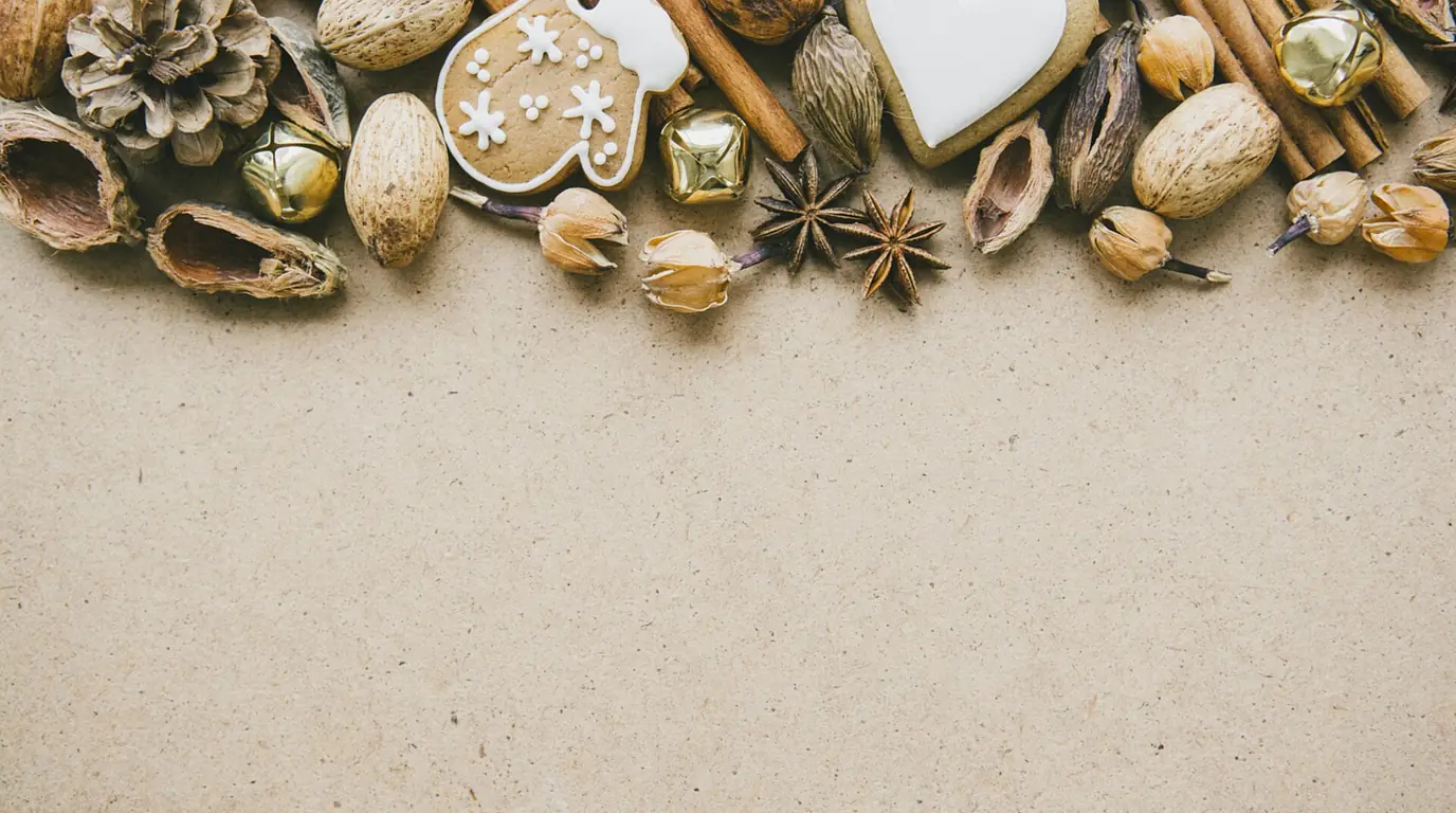 Walnuts, pine cones, star anise, cinnamon sticks, small bells and iced gingerbread biscuits along the top of a pale table