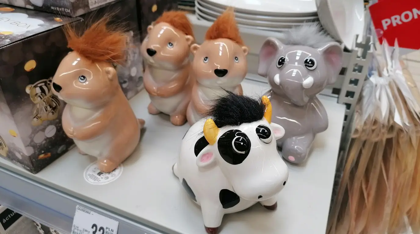 Ceramic piggy banks shaped like hamsters, a cow and an elephant on a shop shelf.