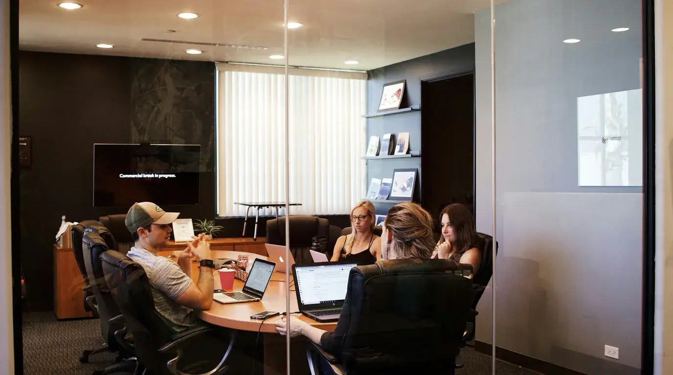 A meeting room with wall screens and people working at laptops