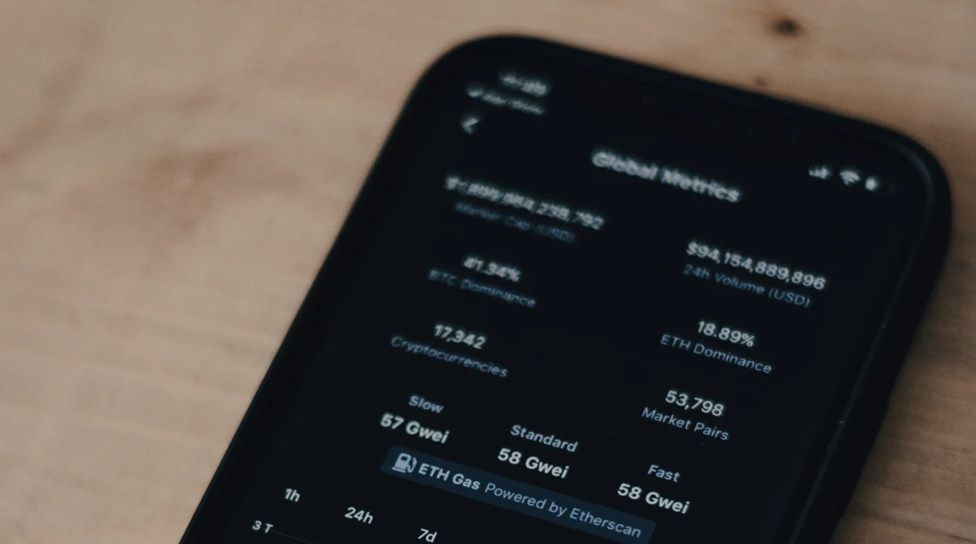 Dark phone screen showing a grid of market figures and percentages, resting on a pale wooden surface.
