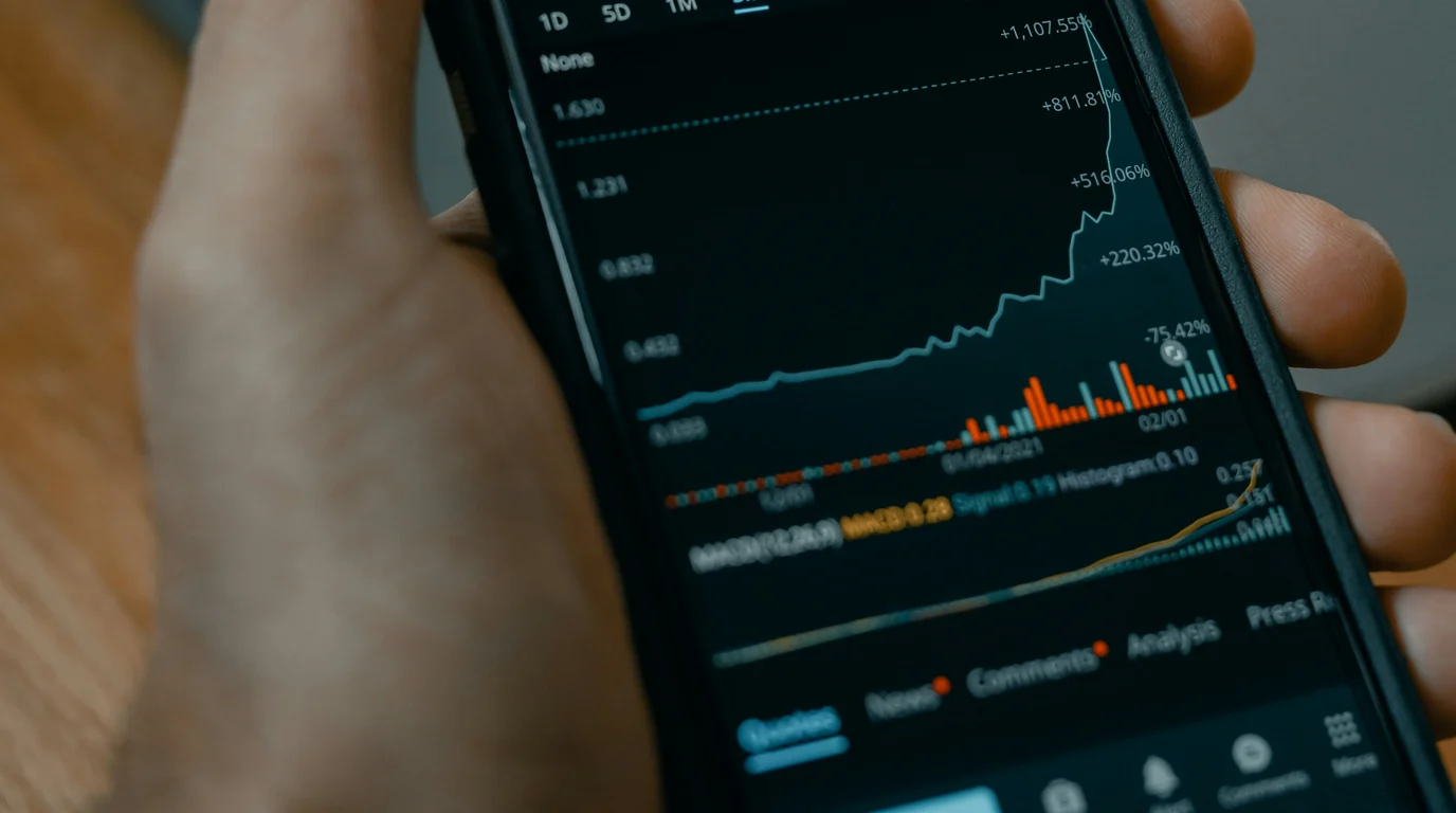 Close view of a phone held in one hand, its dark screen filled with a steeply rising line chart and coloured bars.