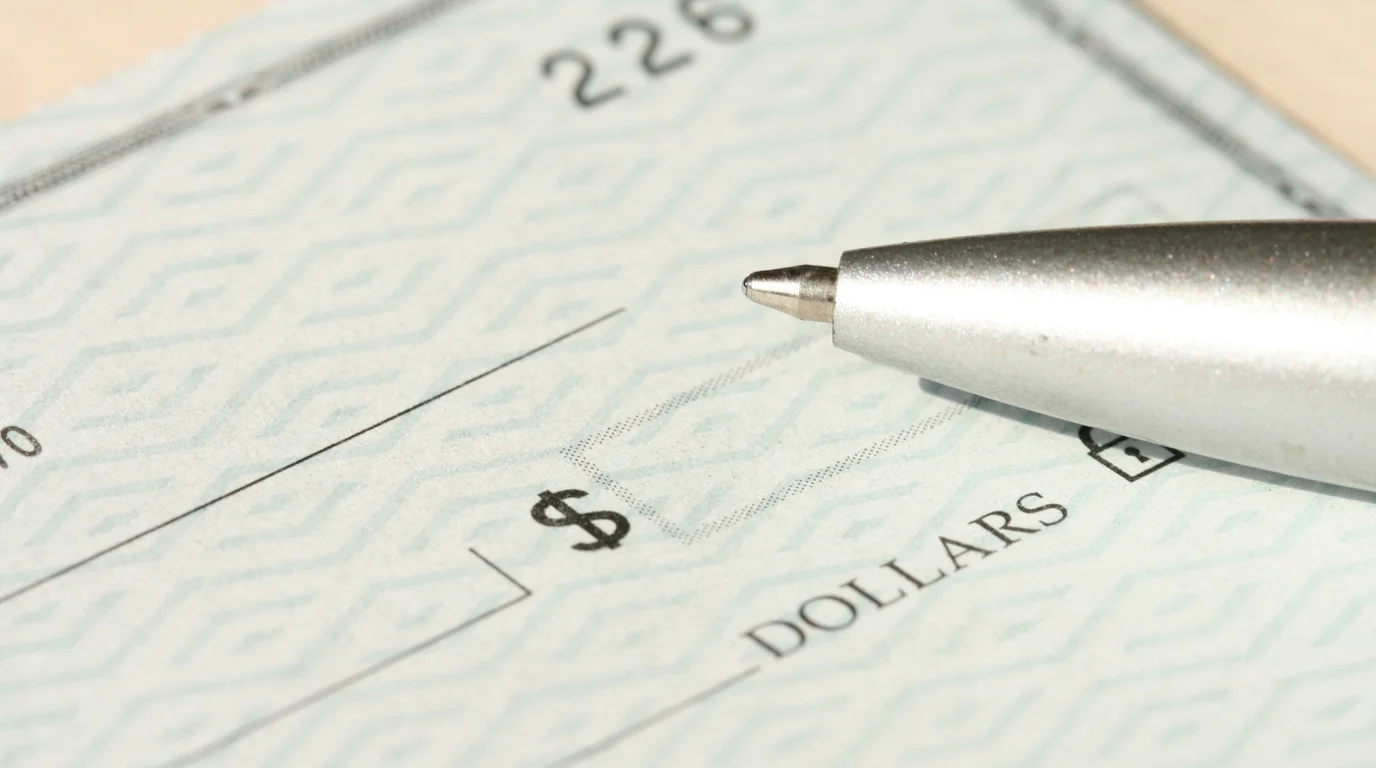 Silver ballpoint pen resting on a blank patterned cheque, its amount box and printed 'dollars' line in sharp focus.