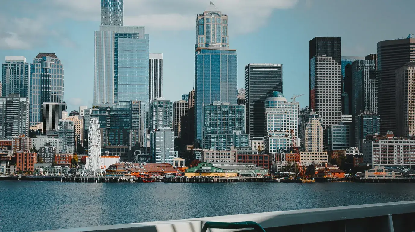 A waterfront city skyline seen from the water, a white Ferris wheel on the pier below the towers.